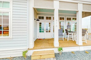 A white house with a wooden porch, a dining area with a table and chairs, and a small garden with gravel and plants. - Palmilla Beach Resort-416 Mermaid Tail Lane (Port Aransas)
