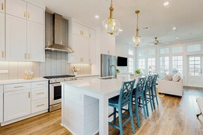 A modern kitchen with white cabinetry, a central island, and blue chairs. - Palmilla Beach Resort-416 Mermaid Tail Lane (Port Aransas)
