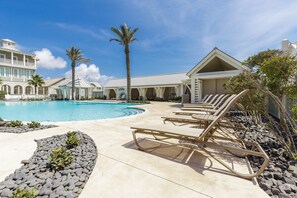 A pool area with lounge chairs, a large pool, and a building with a white exterior and arched windows. - Palmilla Beach Resort-423 Mermaid Tail Lane (Port Aransas)