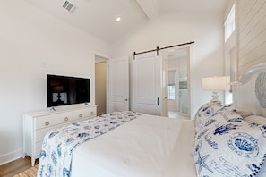 A bedroom with a bed, a TV, a dresser, and a door leading to another room. - Palmilla Beach Resort-423 Mermaid Tail Lane (Port Aransas)
