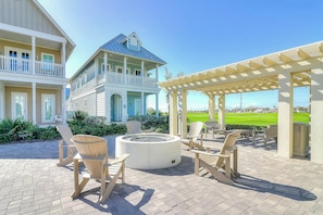 A two-story house with a balcony, outdoor seating area with chairs and a fire pit, and a view of a golf course. - Palmilla Beach Resort-427 Mermaid Tail Lane (Port Aransas)