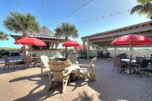 An outdoor seating area with tables and chairs, red umbrellas, and a bar area with a sign reading 'REDS'. - Palmilla Beach Resort-602 Sunset Avenue (Port Aransas)