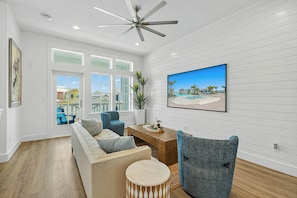 A spacious living room with a high ceiling fan, a large window with a view of the outside, a comfortable sofa set, and a wooden coffee table. - Palmilla Beach Resort-602 Sunset Avenue (Port Aransas)