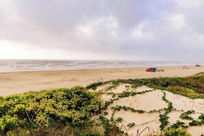En strand med sanddynor, vegetation och ett fordon med ett tält.