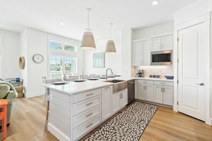 A modern kitchen with white cabinetry, a large island, pendant lighting, and a view to the outdoors. - Palmilla Beach Resort-604 Sunset Avenue (Port Aransas)