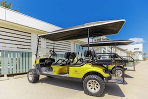 A yellow golf cart parked in front of a building with a white facade and a covered area. - Palmilla Beach Resort-604 Sunset Avenue (Port Aransas)