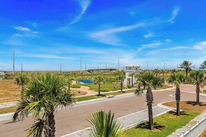 A coastal road with palm trees, a small pool, and a distant bridge. - Palmilla Beach Resort-606 Sunset Avenue (Port Aransas)