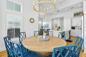 A modern kitchen with white cabinets, a central island, and a dining area with blue chairs and a wooden table. - Palmilla Beach Resort-627 Sunset Avenue (Port Aransas)