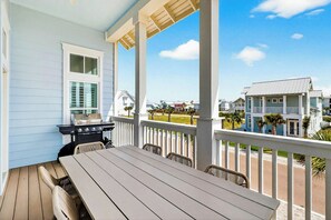 Een overdekt buitengebied met een tafel en stoelen, een barbecue en uitzicht op een woonwijk met huizen.