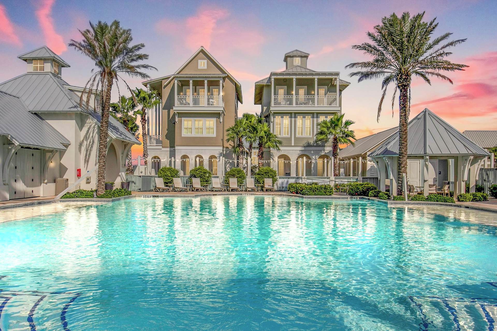 A resort with a large swimming pool, multiple buildings with balconies, and palm trees.