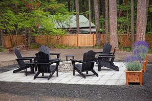 Eine Terrasse mit vier Adirondack-Stühlen, einer kleinen Feuerstelle und einem Holzpflanzgefäß mit Lavendel.