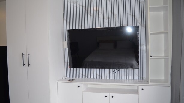 Quarto com cama, televisão presa à parede e guarda-roupa com duas portas.