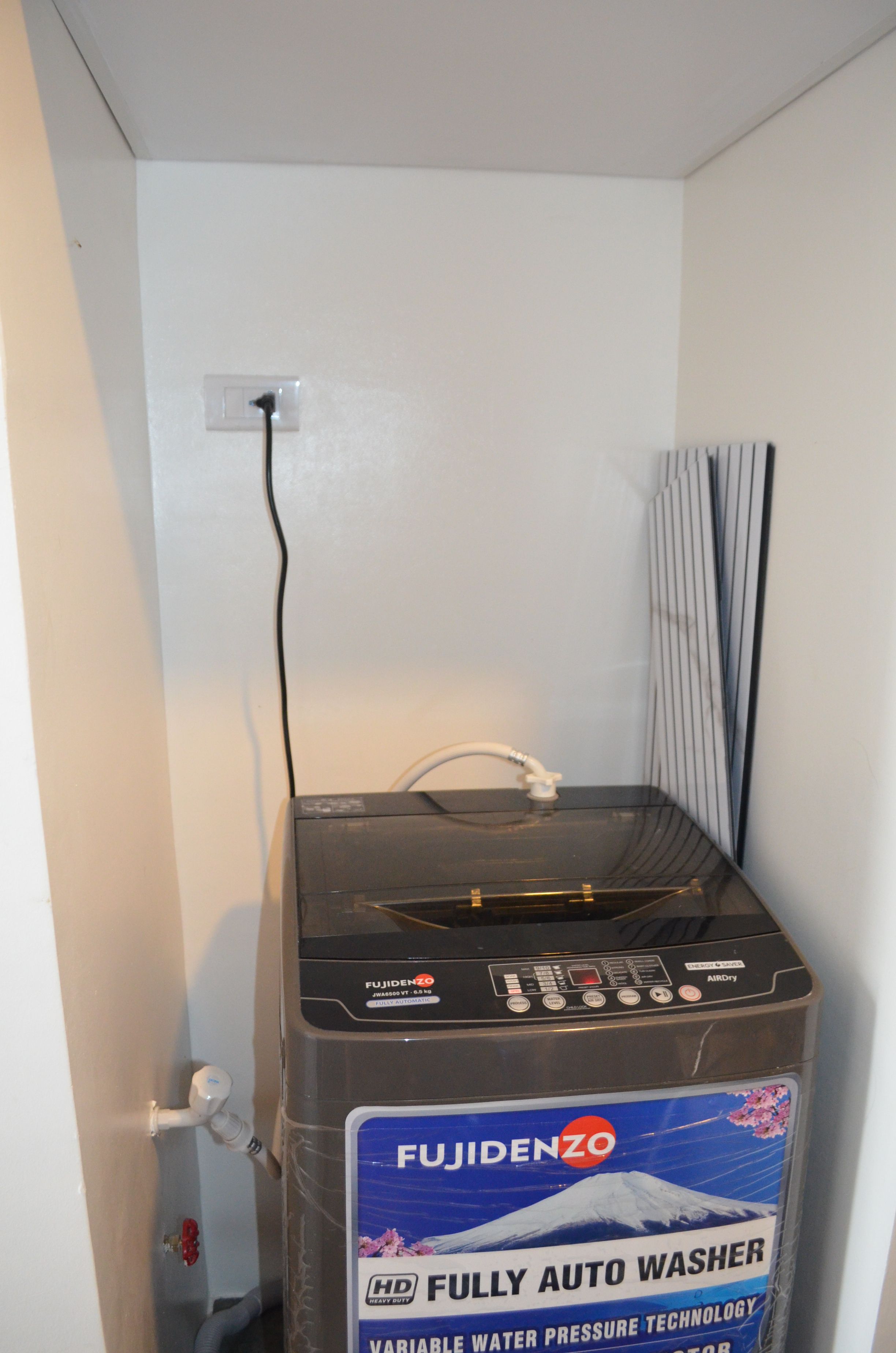 Eine vollautomatische Waschmaschine mit Technologie zur Optimierung des Wasserdrucks, platziert in einem Raum mit weißer Wand und einem Fenster mit Jalousien.
