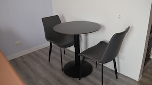 Uma pequena mesa redonda com duas cadeiras, parede em tom claro e piso de madeira.