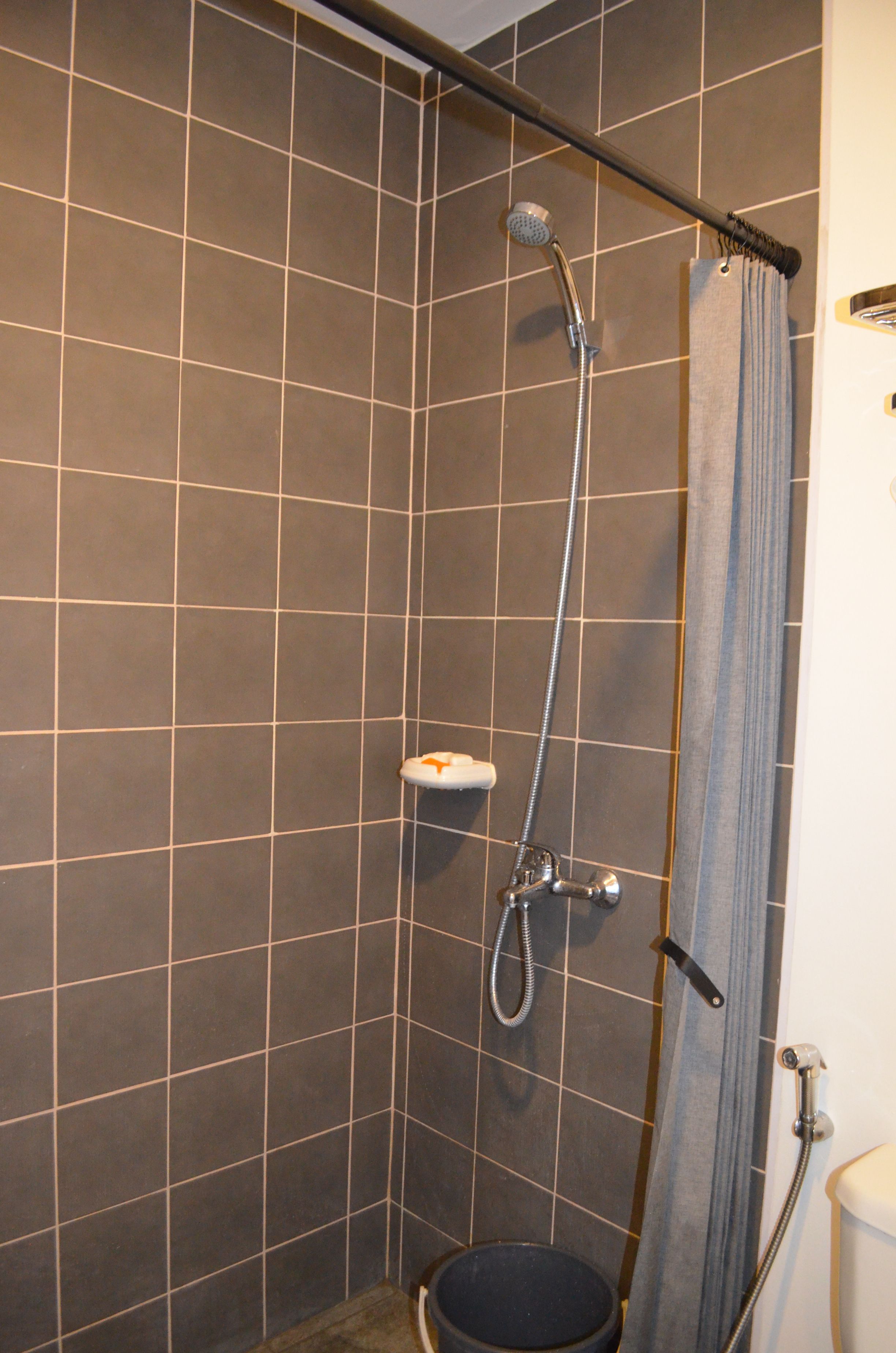 Suihkutila, jossa on käsisuihkusetti, seinään asennettu hana ja wc.