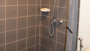 Área de chuveiro com chuveiro manual, torneira fixada na parede e vaso sanitário.