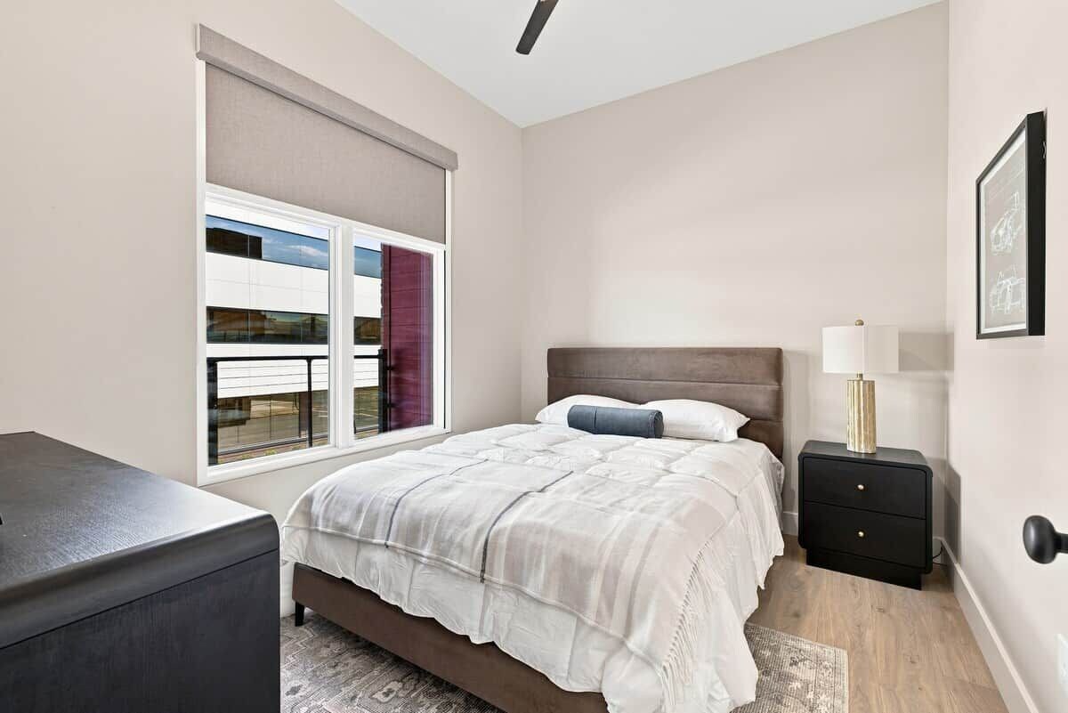 A bedroom with a bed, bedside table, and a window with blinds.