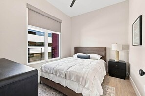 A bedroom with a bed, bedside table, and a window with blinds. - The Paddock · 2 Bed · 2 Bath · 1100 SF (Owensboro)