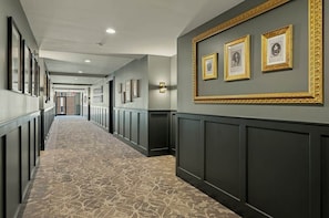 A hallway with a patterned carpet, dark wall paneling, and framed pictures on the wall. - The Paddock · 2 Bed · 2 Bath · 1100 SF (Owensboro)