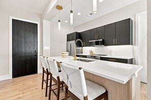 A modern kitchen with a central island, dark cabinetry, and pendant lighting.