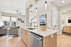 A modern kitchen with a central island, built-in dishwasher, pendant lighting, and a large window.