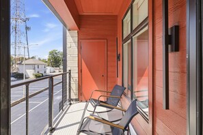 A balcony with two chairs, a glass door, and a view of a parking lot and buildings.