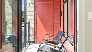 A narrow balcony with a red door, glass railings, and two black chairs. - The Oaks · 2 Bedroom · 2 Bath · 1400SF (Owensboro)