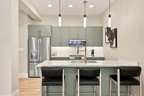 A modern kitchen with a central island, stainless steel appliances, and bar stools. - The Oaks · 2 Bedroom · 2 Bath · 1400SF (Owensboro)