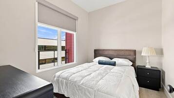 Un dormitorio con cama, mesita de noche, lámpara y ventana con persianas.