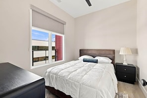 Un dormitorio con cama, mesita de noche, lámpara y ventana con persianas.