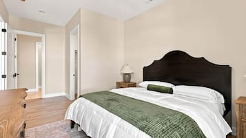 Un dormitorio con una cama grande, una mesita de noche con lámpara y un aparador de madera.