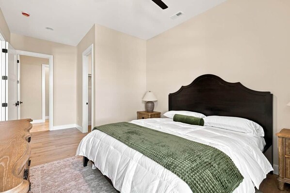 Un dormitorio con una cama grande, una mesita de noche con lámpara y un aparador de madera.