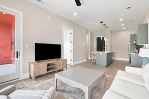 Una sala moderna con un televisor de pantalla plana, una mesa de centro y un sofá. Cuenta con una zona de cocina con una mesa y sillas.