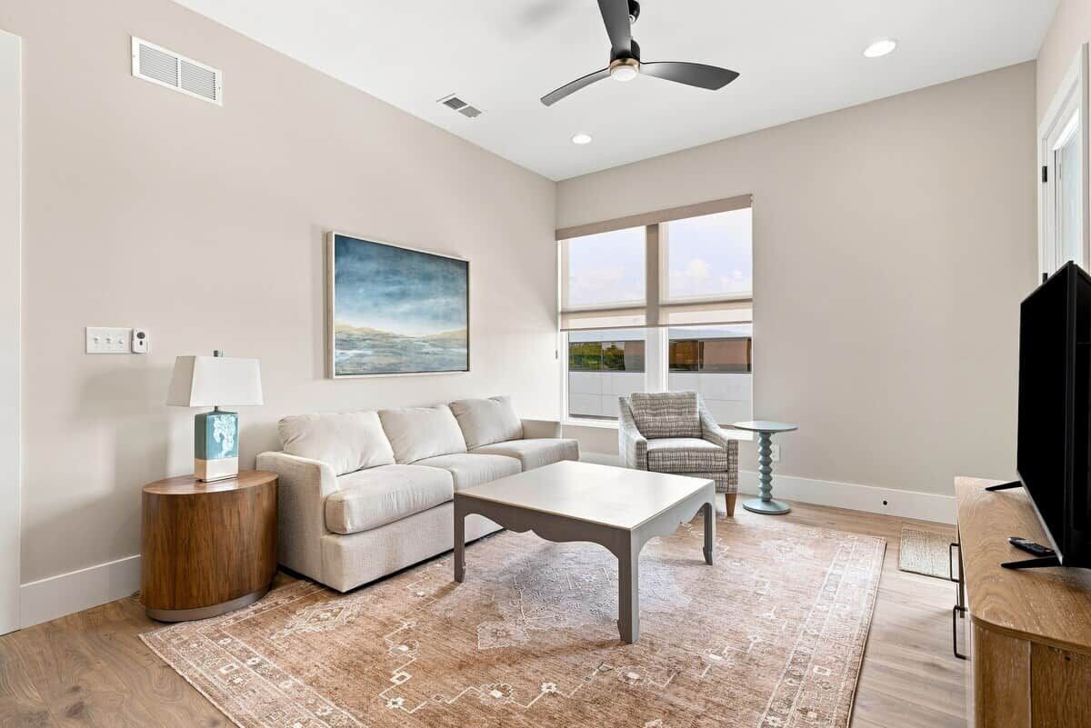 A living room with a sofa, coffee table, and a chair. There is a painting on the wall, a lamp, and a television.