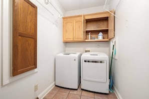 A laundry room with two white front-loading washing machines, a wooden cabinet above, and a mop leaning against the wall. - Laney’s Lake Retreat (Northport)