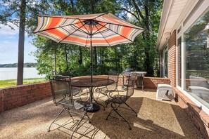 An outdoor patio with a metal table and chairs, a striped umbrella, and a grill. - Laney’s Lake Retreat (Northport)