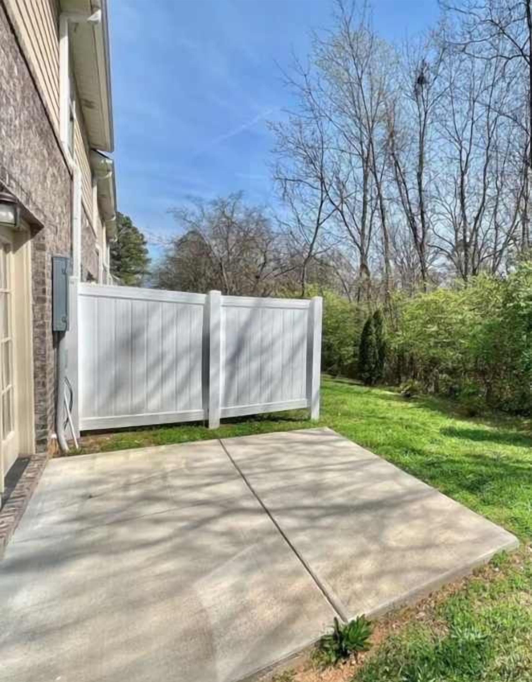 Una propiedad residencial con entrada de concreto, cerca blanca y césped bien cuidado.