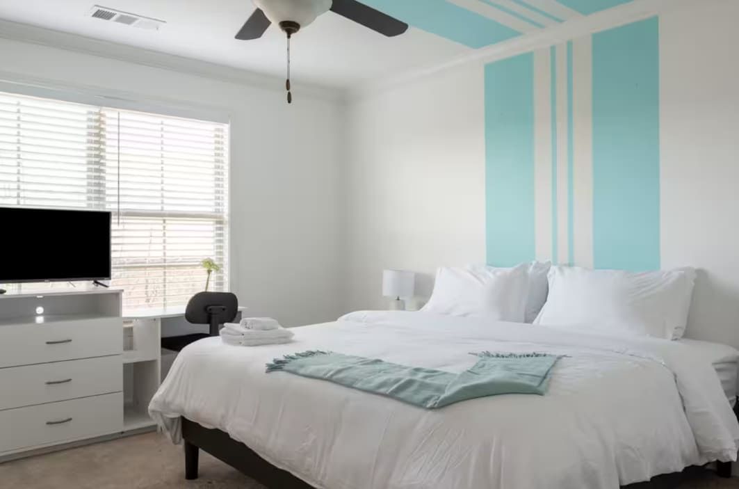 A hotel room with a bed, a desk, a television, and a ceiling fan.