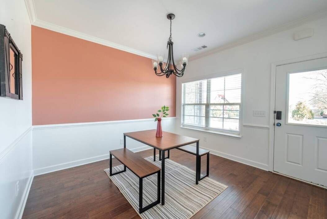 A room with a wooden table and bench, a chandelier, a window with blinds, and a door.