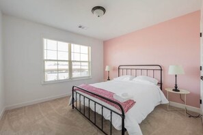 A bedroom with a single bed, two bedside lamps, a window, and a pink accent wall.