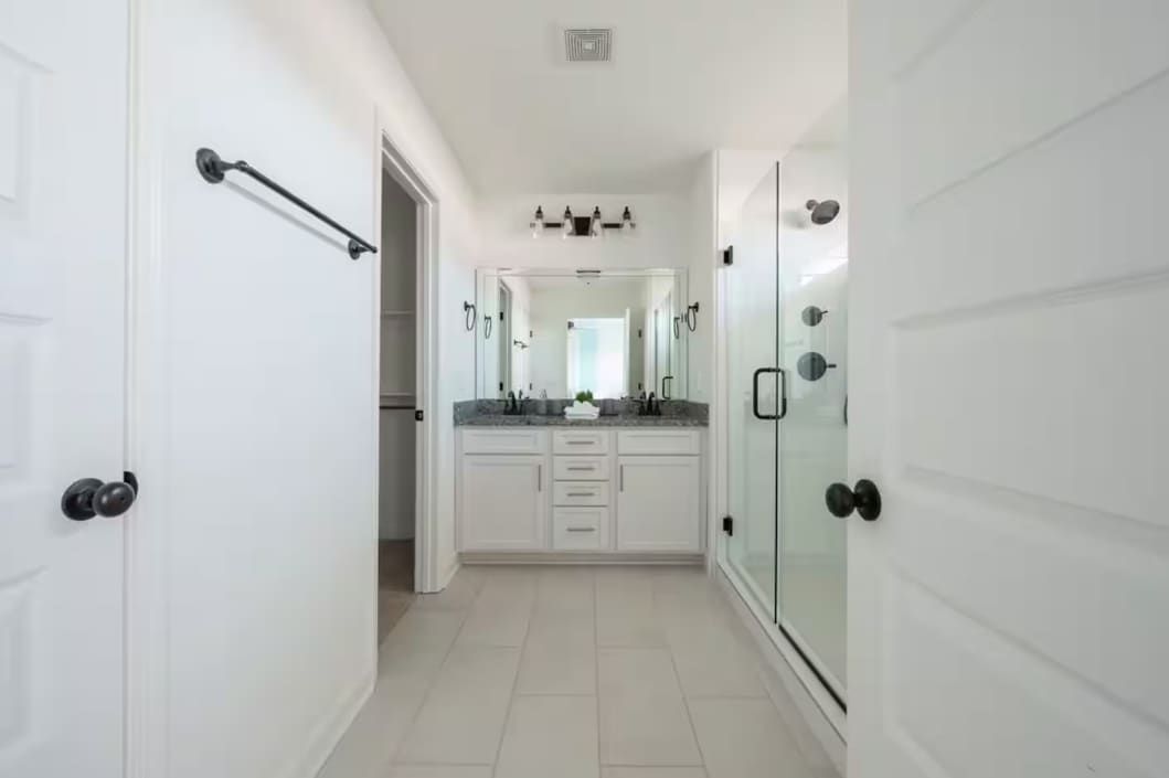 A hallway leading to a bathroom with a glass shower enclosure and a vanity with a mirror.
