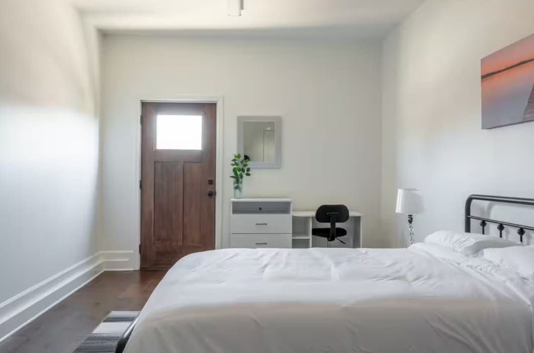 Un dormitorio con cama, escritorio, silla, cómoda y una puerta.