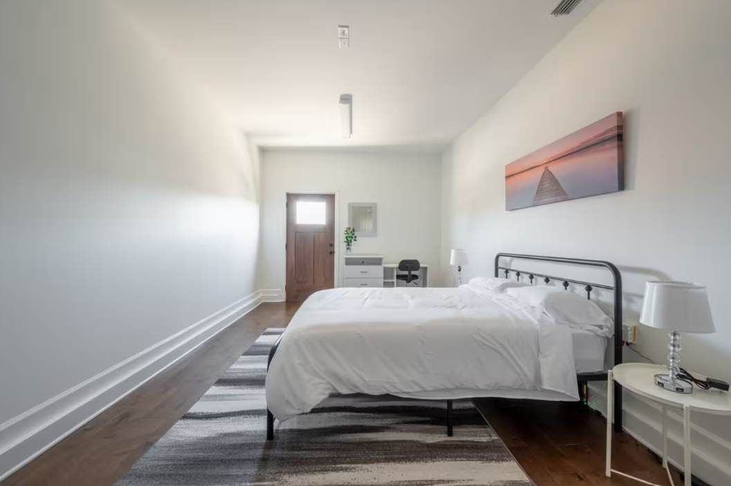 A bedroom with a bed, bedside table, and a painting on the wall.