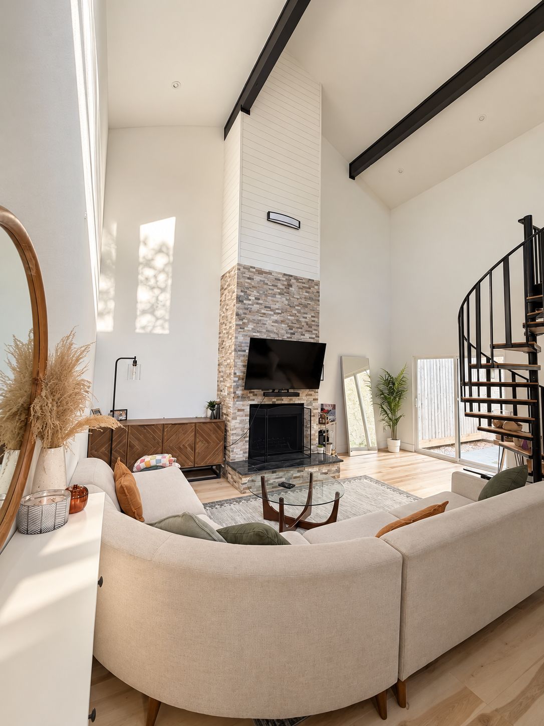 Amplia sala de estar con chimenea, un televisor de pantalla plana grande, un sofá curvo y una escalera espiral.