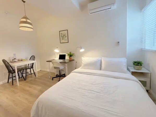 A bedroom with a bed, a desk with a laptop, a chair, and a hanging light fixture.