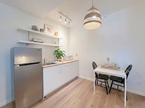 A modern kitchen with a stainless steel refrigerator, white cabinets, a wooden countertop, and a dining table with chairs.