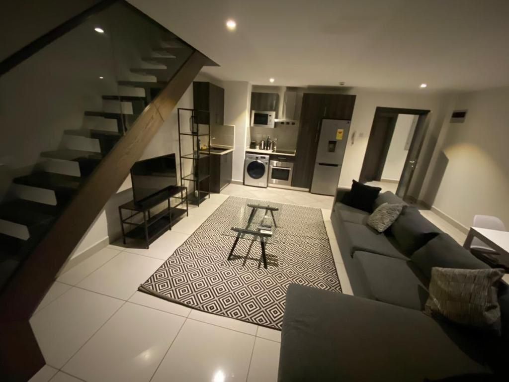 A modern living space with a staircase, a kitchen, and a seating area.