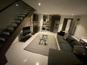 A modern living space with a staircase, a kitchen, and a seating area. - Ebs properties Africa limited  (Accra)