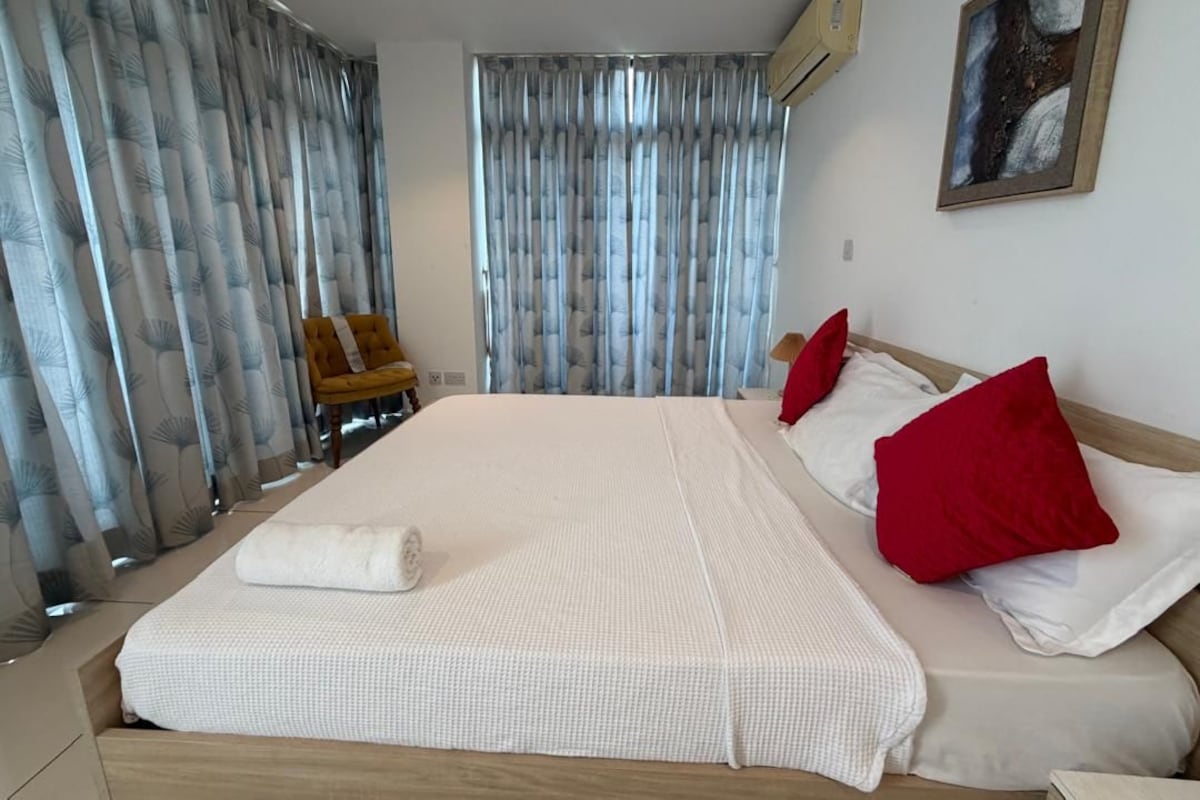 Ett hotellrum med en stor säng, två röda kuddar, en vit filt och en tavla på väggen.