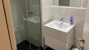 Un baño con ducha envuelta en vidrio, un lavamanos blanco y un espejo encima.